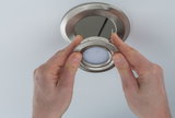 Hands installing round brushed stainless steel recessed spotlight in white ceiling for LED lighting