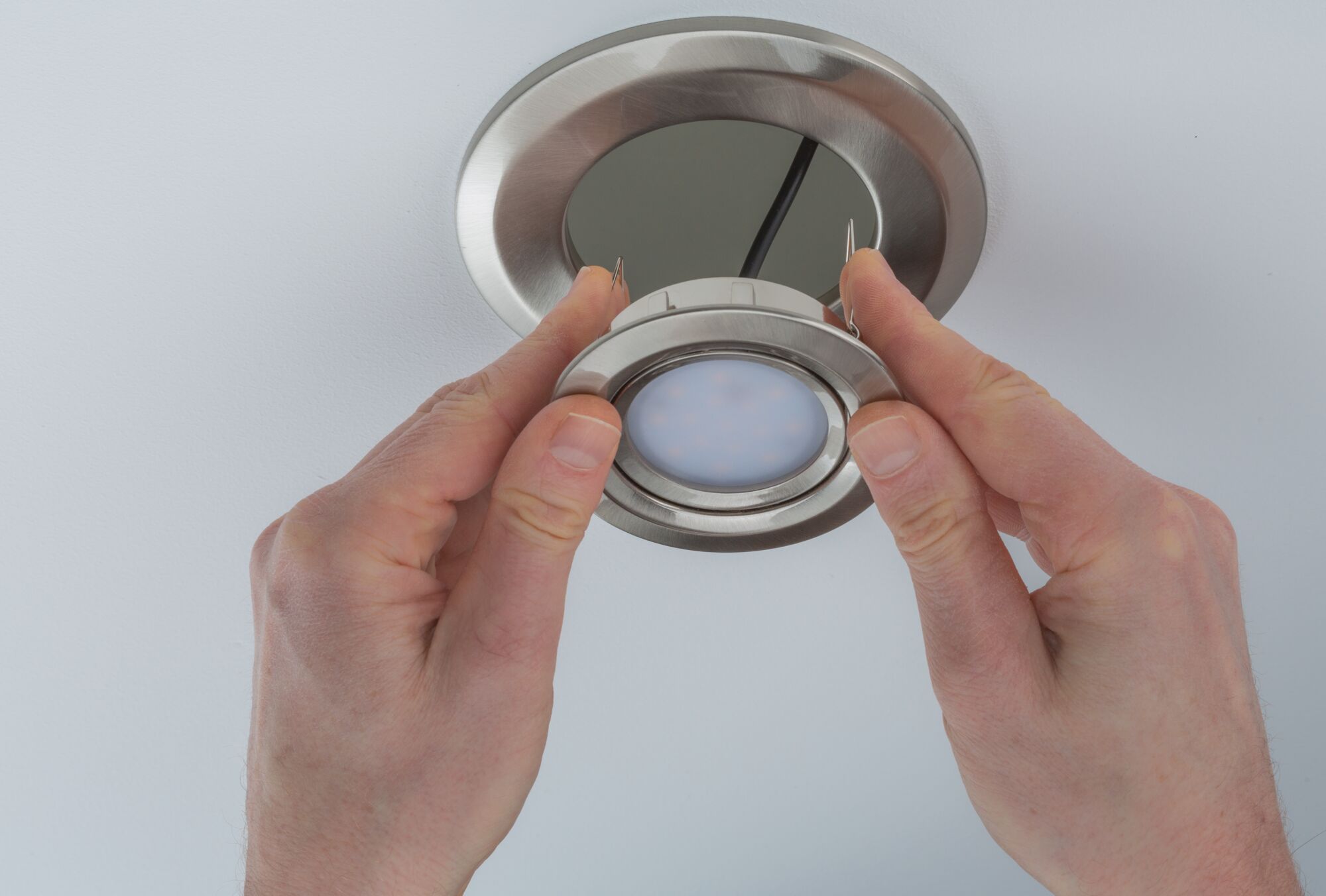 Mains installant un spot encastré rond en acier inoxydable brossé dans un plafond blanc pour éclairage LED