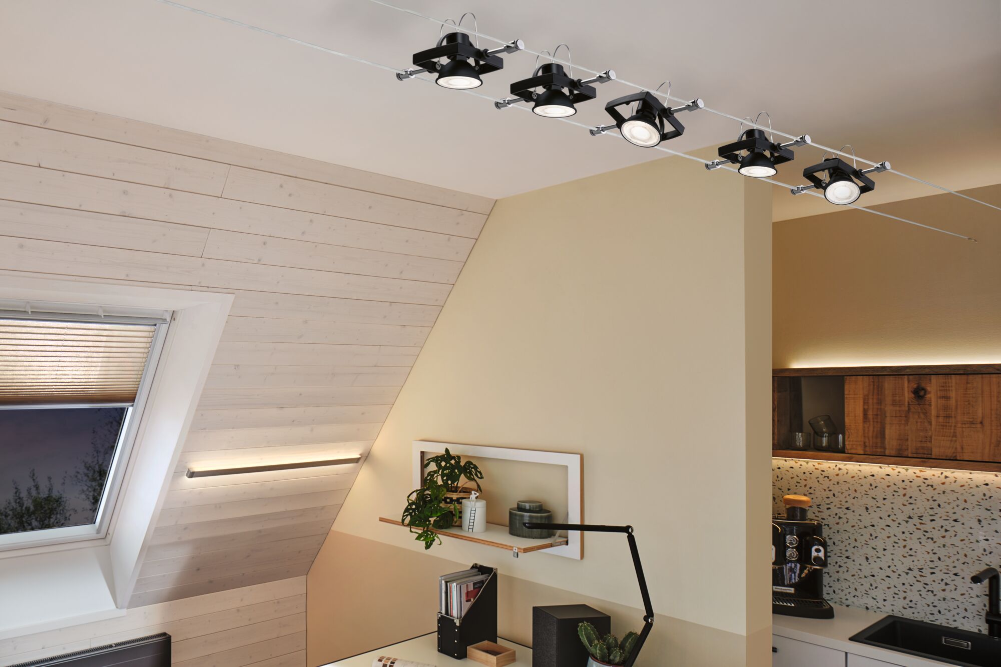 Zwarte LED-kabelspots met verstelbare koppen in moderne woonruimte met houten bekleding en werkplek.