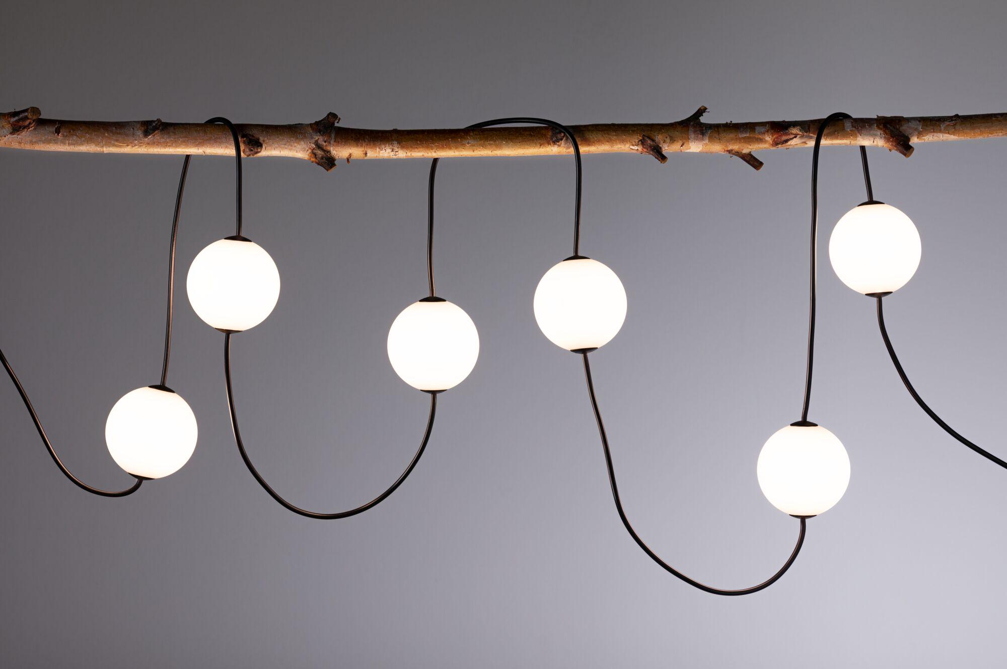 Guirlande LED moderne avec globes blancs sur câble noir suspendue décorativement à une branche en bois