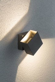 Modern black aluminium wall spotlight with warm white light on textured wall for outdoor lighting