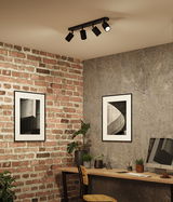 Black metal ceiling spotlights with four adjustable lamps in modern workspace with brick wall and desk