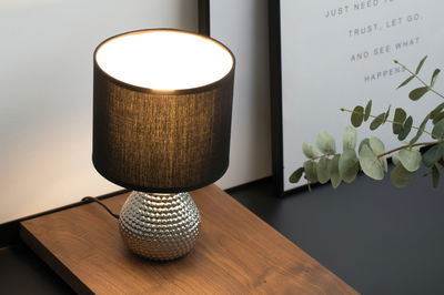 Table lamp with black fabric shade and silver textured metal base on wooden surface