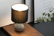 Table lamp with black fabric shade and silver textured ceramic base on wooden surface