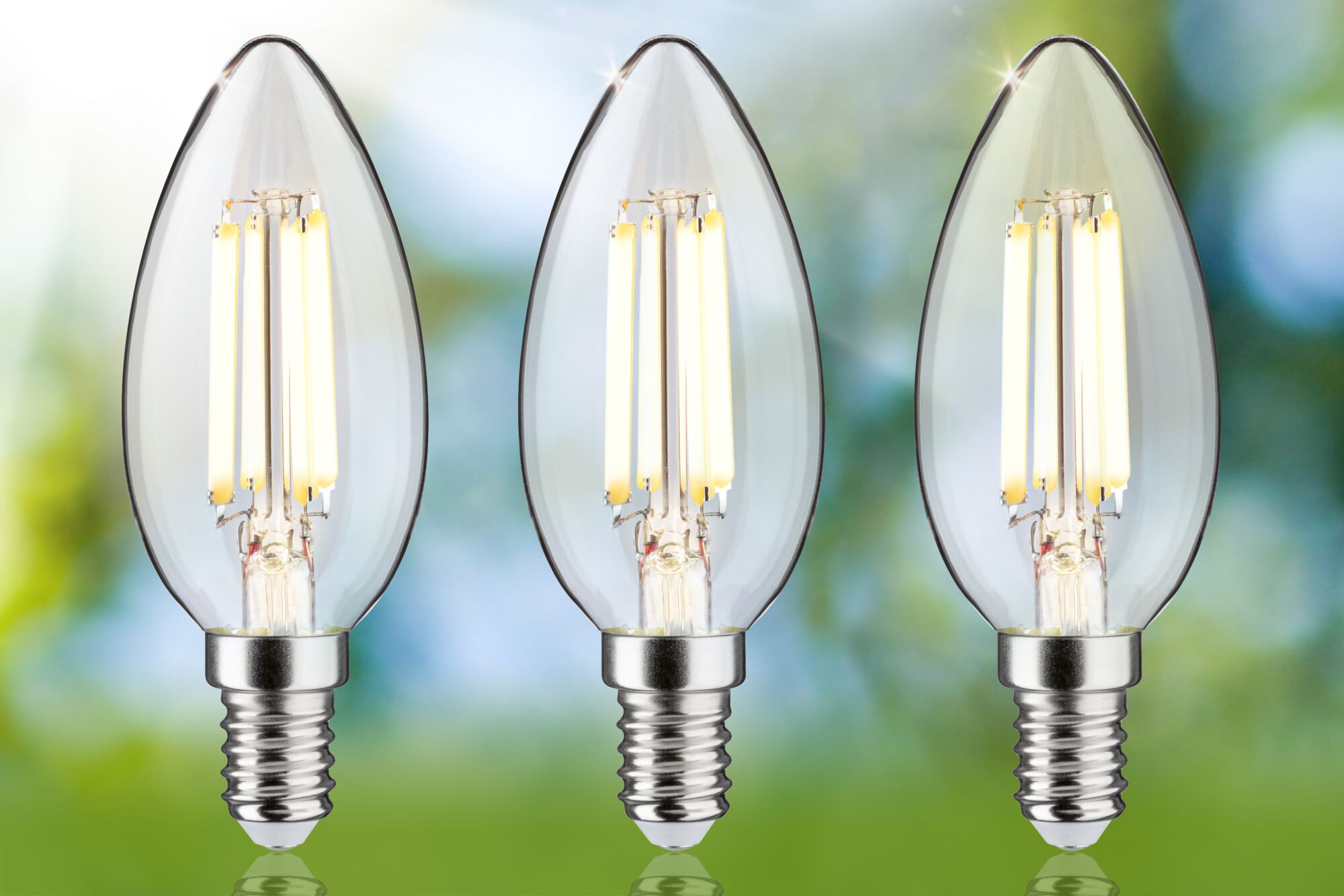 Drei klare LED-Kerzenlampen mit E14-Fassung und warmweißem Licht vor grün-blauem Hintergrund