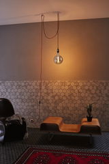 Hanging warm light bulb above modern wooden bench and black chair in hallway with hexagon tiles