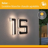Numéro de maison solaire 15 en matériau noir avec lumière LED blanc chaud sur mur gris