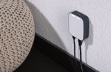 Kompakter weiß-schwarzer Netzwerkadapter an weißer Wand mit zwei Kabeln für Heimnetzwerk.