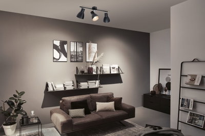 Plafonnier noir à trois spots réglables dans un salon moderne avec canapé marron.