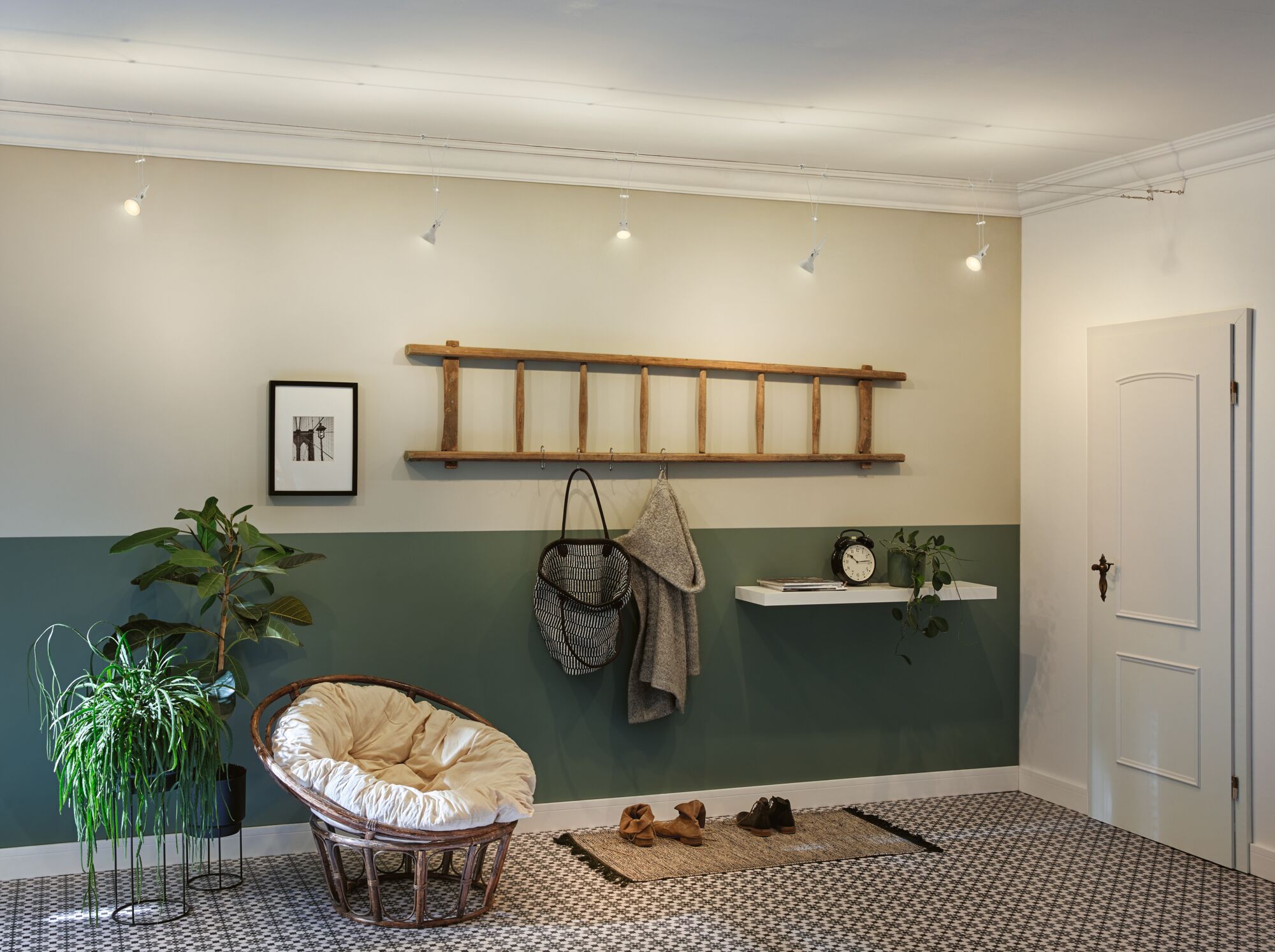 Modern living room with green wall, wooden ladder coat rack, and cozy rattan chair with cushion.