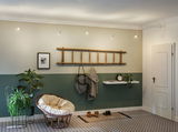 Modern living room with green wall, wooden ladder coat rack, and cozy rattan chair with cushion.