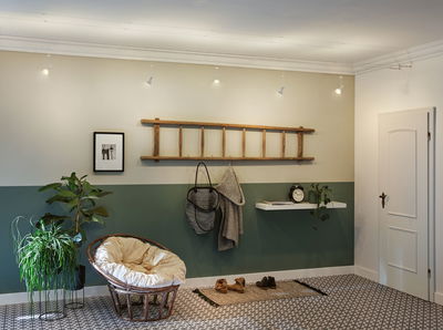 Modern living room with green wall, wooden ladder coat rack, and cozy rattan chair with cushion.