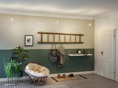 Salon moderne avec mur vert, porte-manteau en échelle en bois et fauteuil en rotin confortable avec coussin.