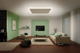 Modern living room with green accent wall, beige sofa, armchair, and rectangular wooden ceiling light.