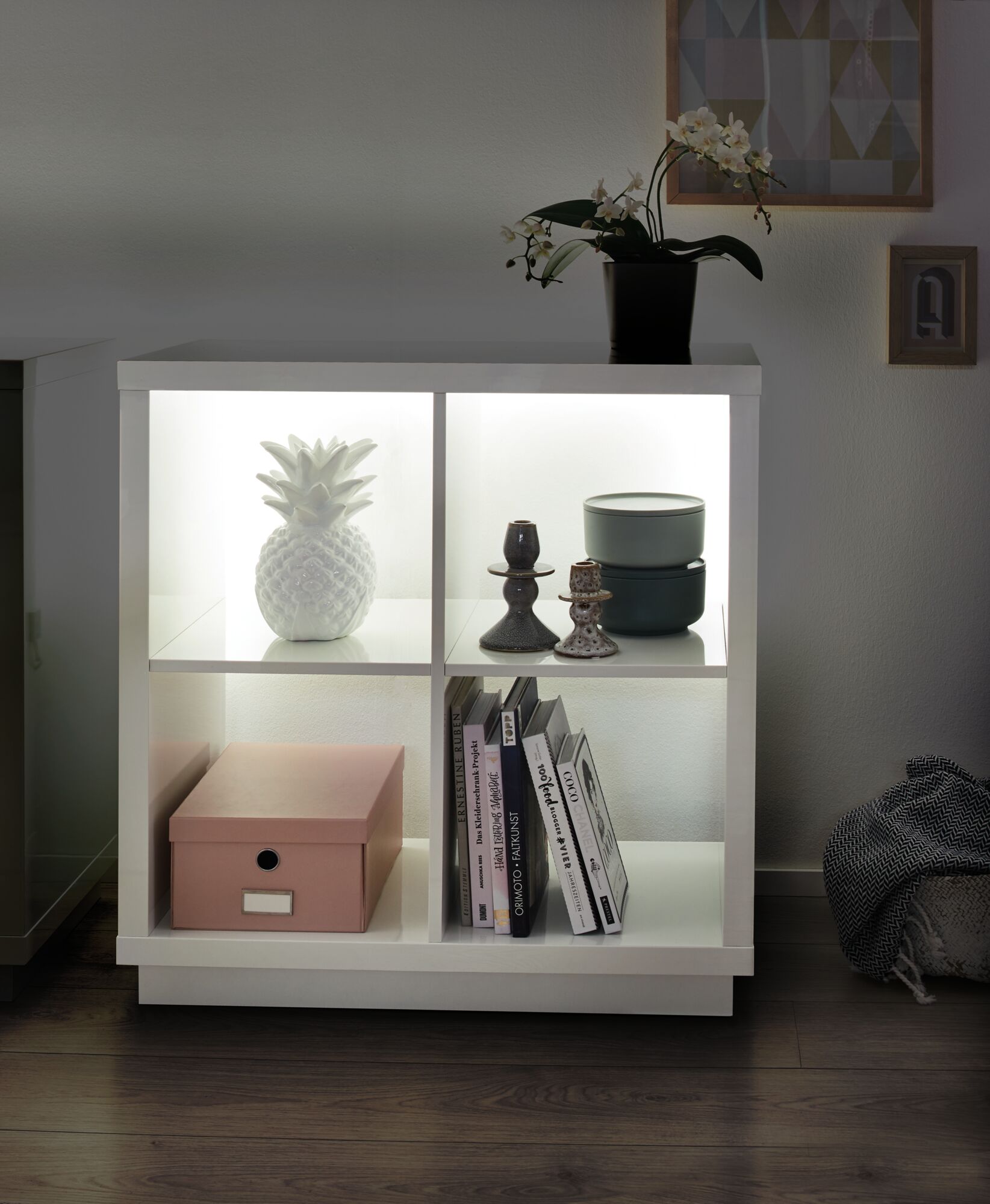 Weißes beleuchtetes Regal mit Keramik-Ananas, Kerzenhaltern und grünen Dosen im modernen Wohnzimmer