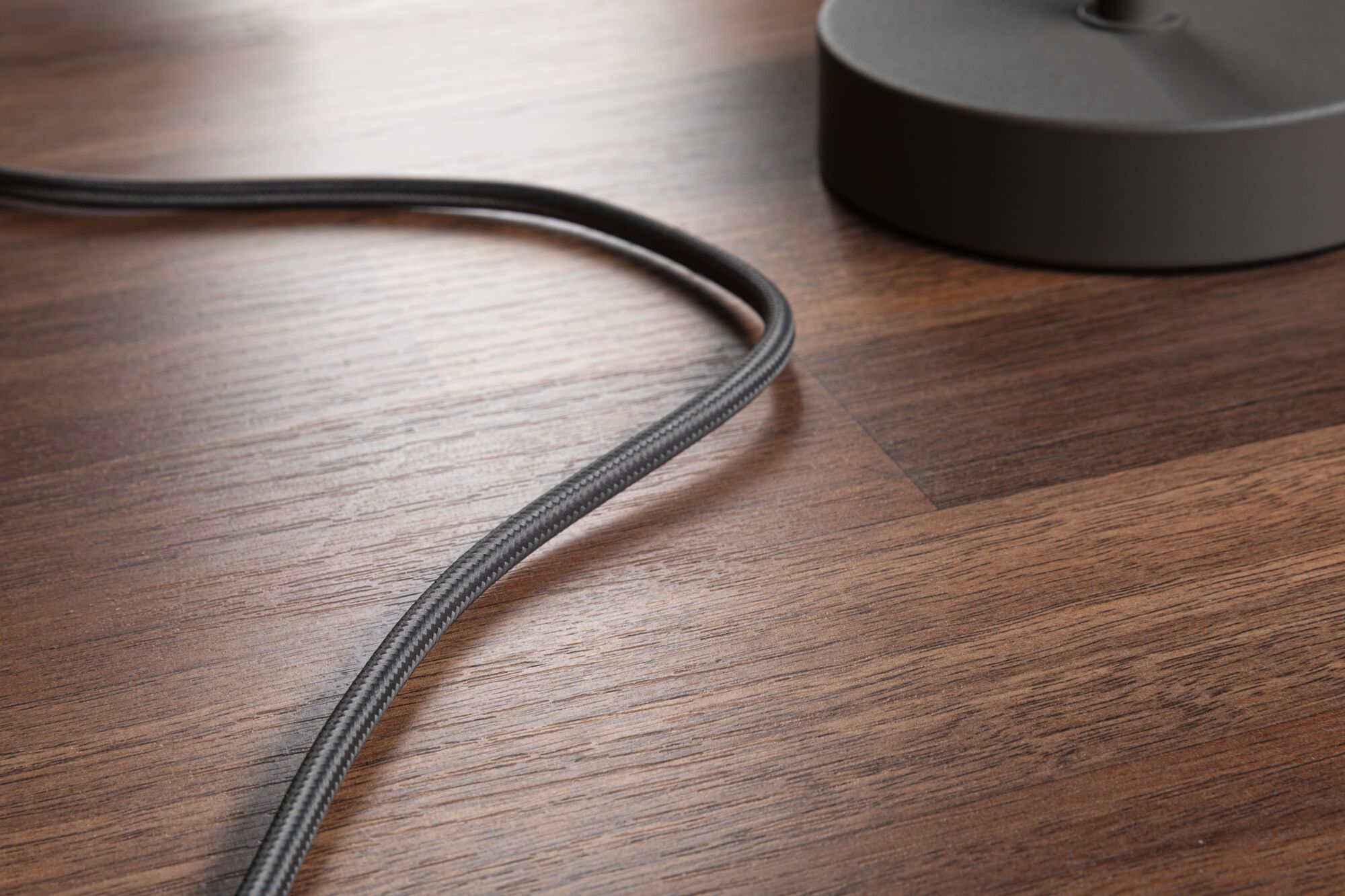 Close-up of black fabric cable on brown wooden floor next to grey lamp base