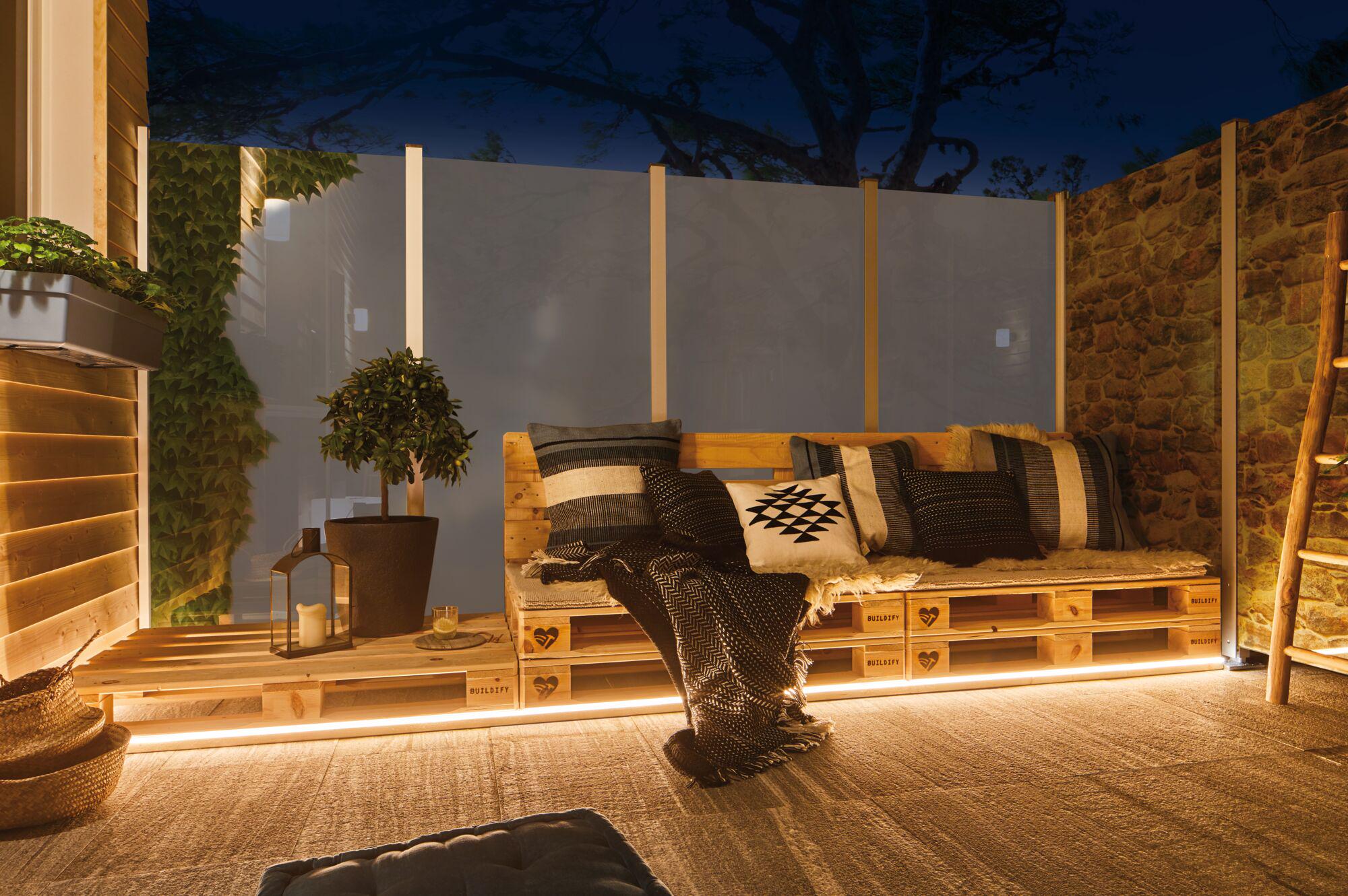 Gezellige buitenlounge met houten palletbank en warm wit LED-licht voor terras en tuin sfeer.