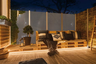 Cozy wooden pallet bench with cushions and LED lighting on terrace at night for outdoor seating