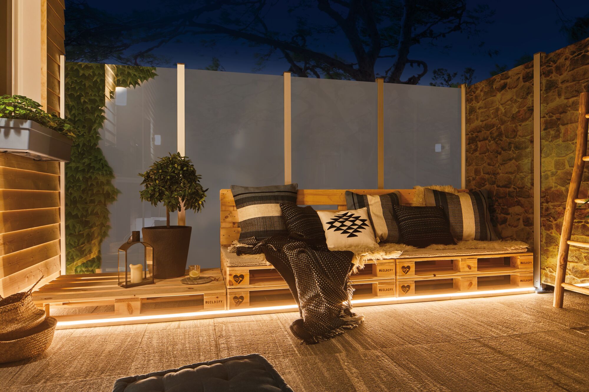 Gezellig houten palletbankje met kussens en LED-verlichting op terras in de avond