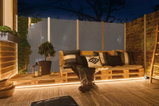 Gemütliche Sitzbank aus Holzpaletten mit Kissen und LED-Beleuchtung auf Terrasse bei Nacht
