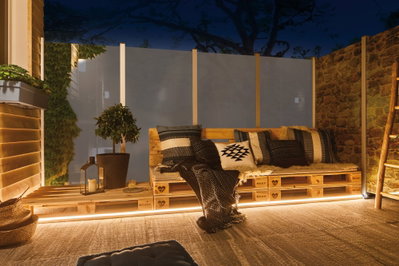 Gemütliche Sitzbank aus Holzpaletten mit Kissen und LED-Beleuchtung auf Terrasse bei Nacht
