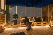 Gemütliche Sitzbank aus Holzpaletten mit Kissen und LED-Beleuchtung auf Terrasse bei Nacht