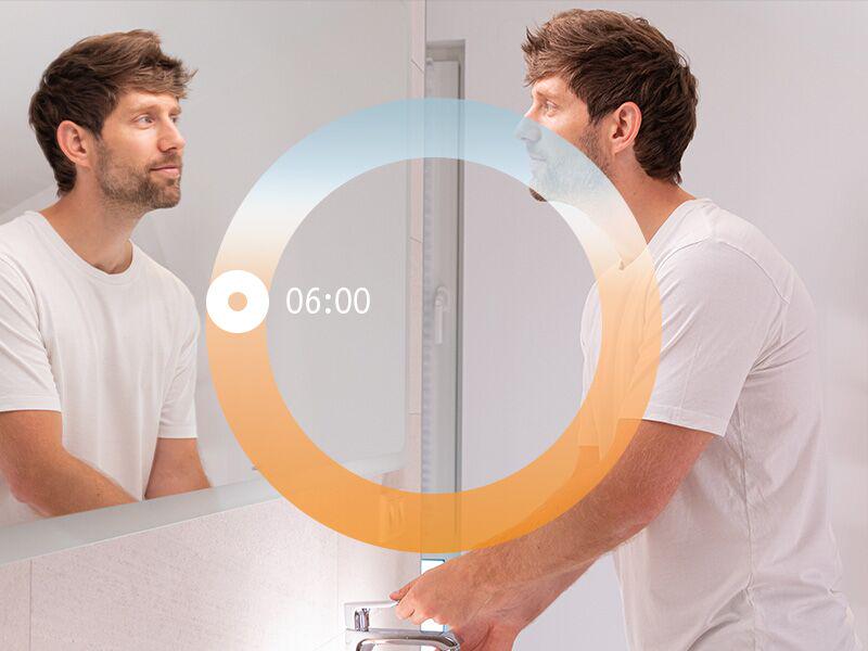 Mann vor Spiegel im Bad mit HCL-Lichtzyklus-Visualisierung für morgendliches Aufstehen um 6 Uhr