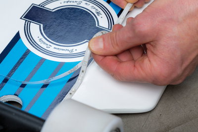 Hand attaching flexible LED strip light on blue and white skateboard with white wheels, LED lighting setup.