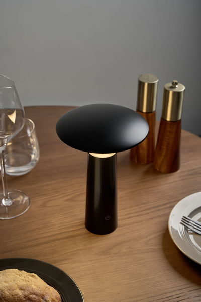 Black metal LED table lamp with round shade on wooden table near dishes and spice mills