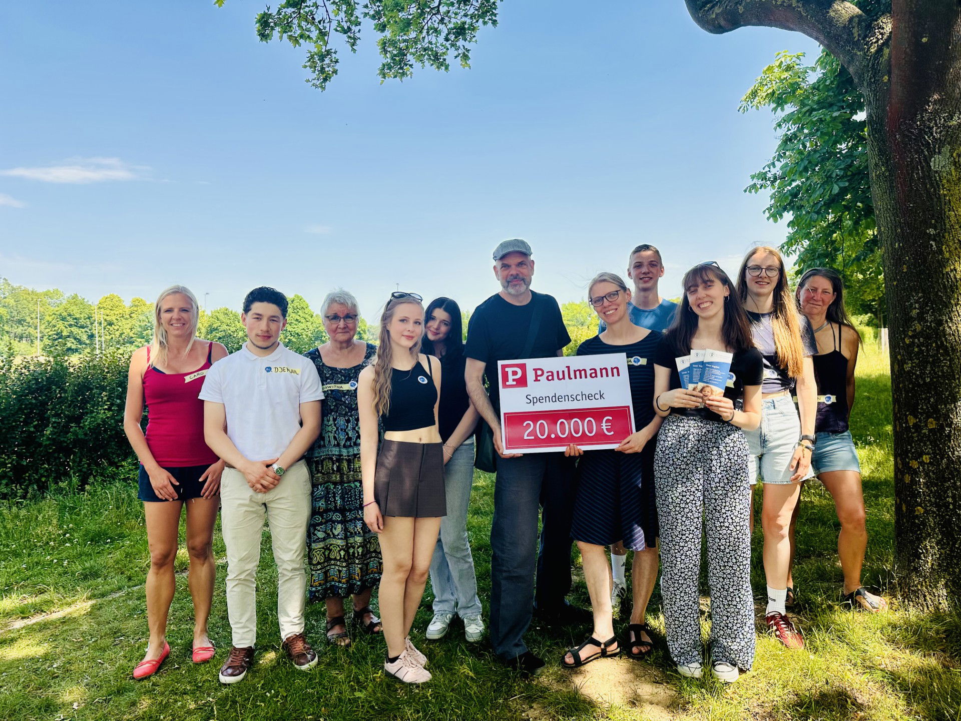 Groep mensen buiten met Paulmann donatiecheque van 20.000 euro op een zonnige dag