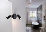 Sort LED-væglampe med to justerbare spots i moderne badeværelse med badekar og trægulv.
