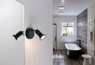 Black LED wall light with two adjustable spots in modern bathroom featuring bathtub and wood floor.