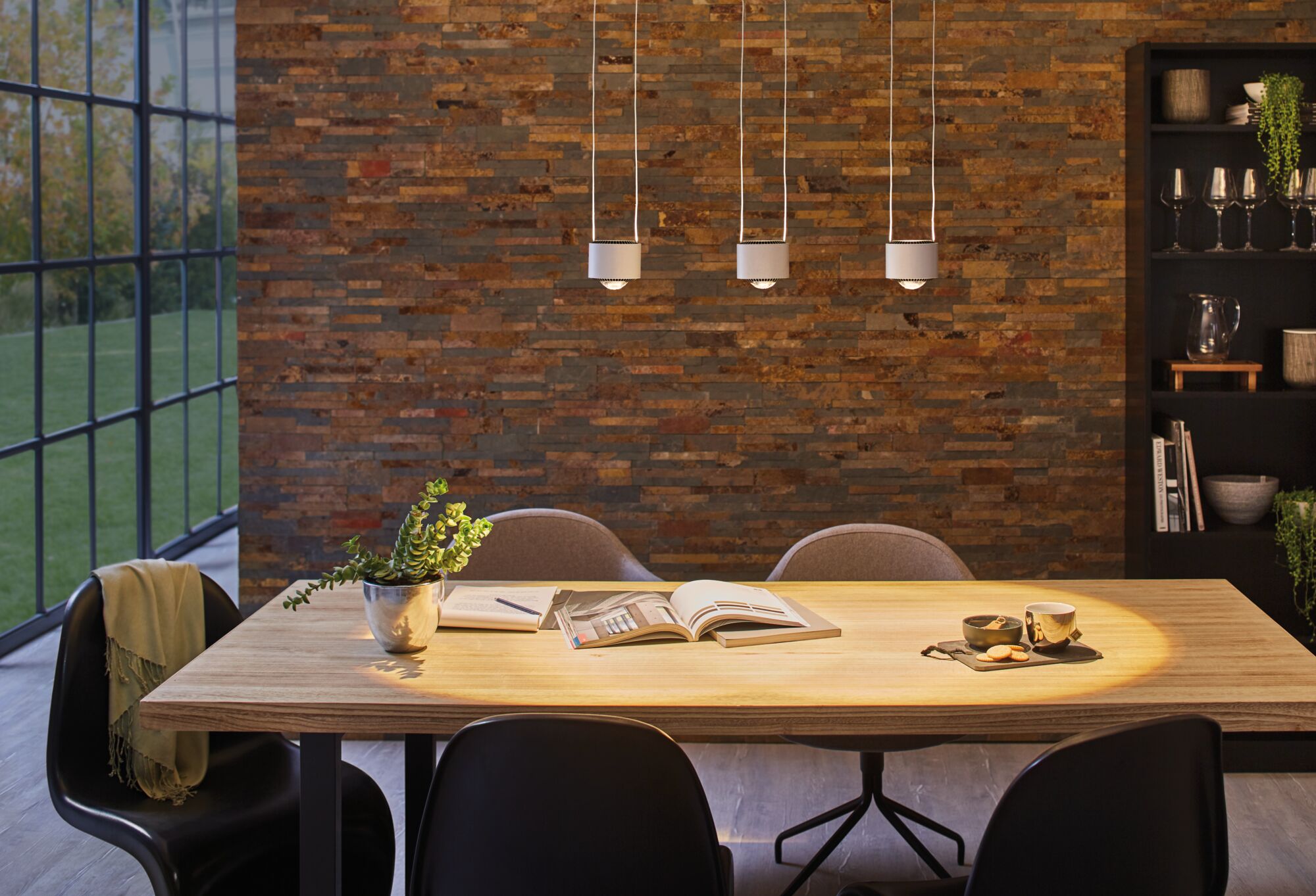 Three white metal LED pendant lights above light wood table with books and plants in dining room
