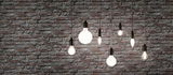 Forskellige filament LED-pærer med varmt hvidt lys foran grå murstensvæg til boligbelysning