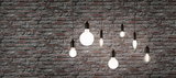 Various filament LED bulbs with warm white light hanging in front of grey brick wall for home lighting