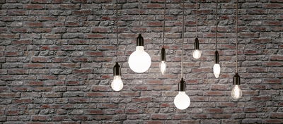 Seven filament light bulbs with black fittings hanging in front of grey brick wall, decorative lighting design.
