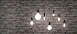 Sieben verschiedene Filament-Glühbirnen mit schwarzer Fassung vor grauer Backsteinwand, Beleuchtung und Design.