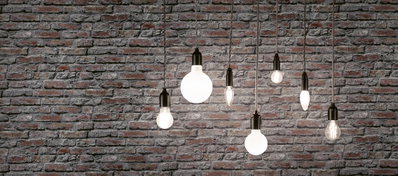 Seven filament light bulbs with black fittings hanging in front of grey brick wall, decorative lighting design.