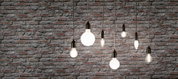 Sept ampoules filament avec douilles noires suspendues devant un mur en briques grises, éclairage décoratif.