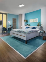 Modernes Schlafzimmer mit weißem Bett, blauem Teppich und quadratischer Deckenleuchte für Wohnraumbeleuchtung