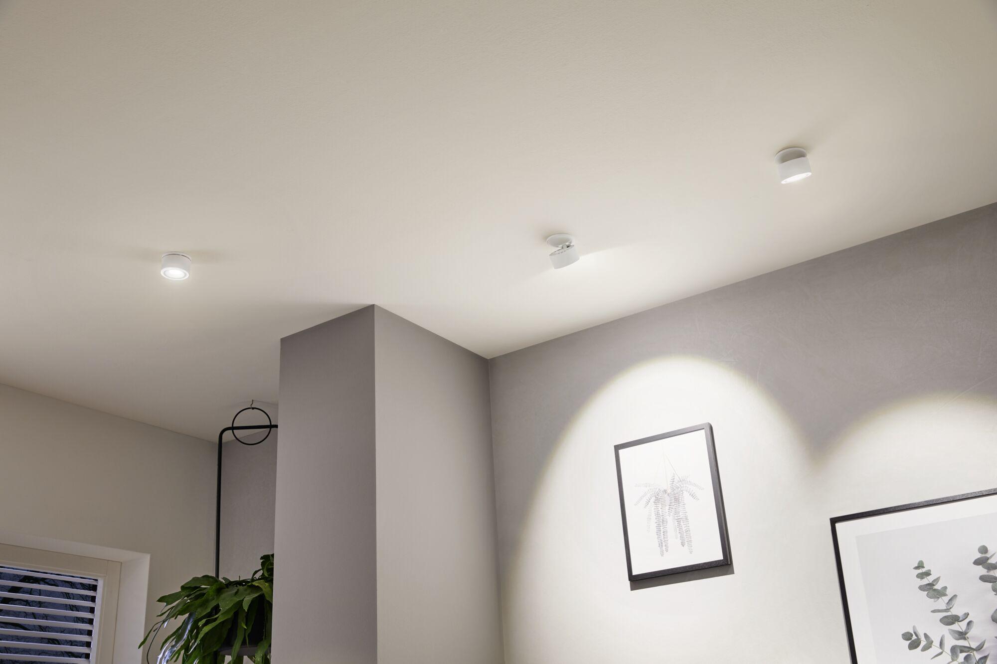 Three white metal LED ceiling spotlights lighting a modern living room corner with pictures and plant