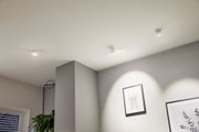 Three white metal LED ceiling spotlights lighting a modern living room corner with pictures and plant