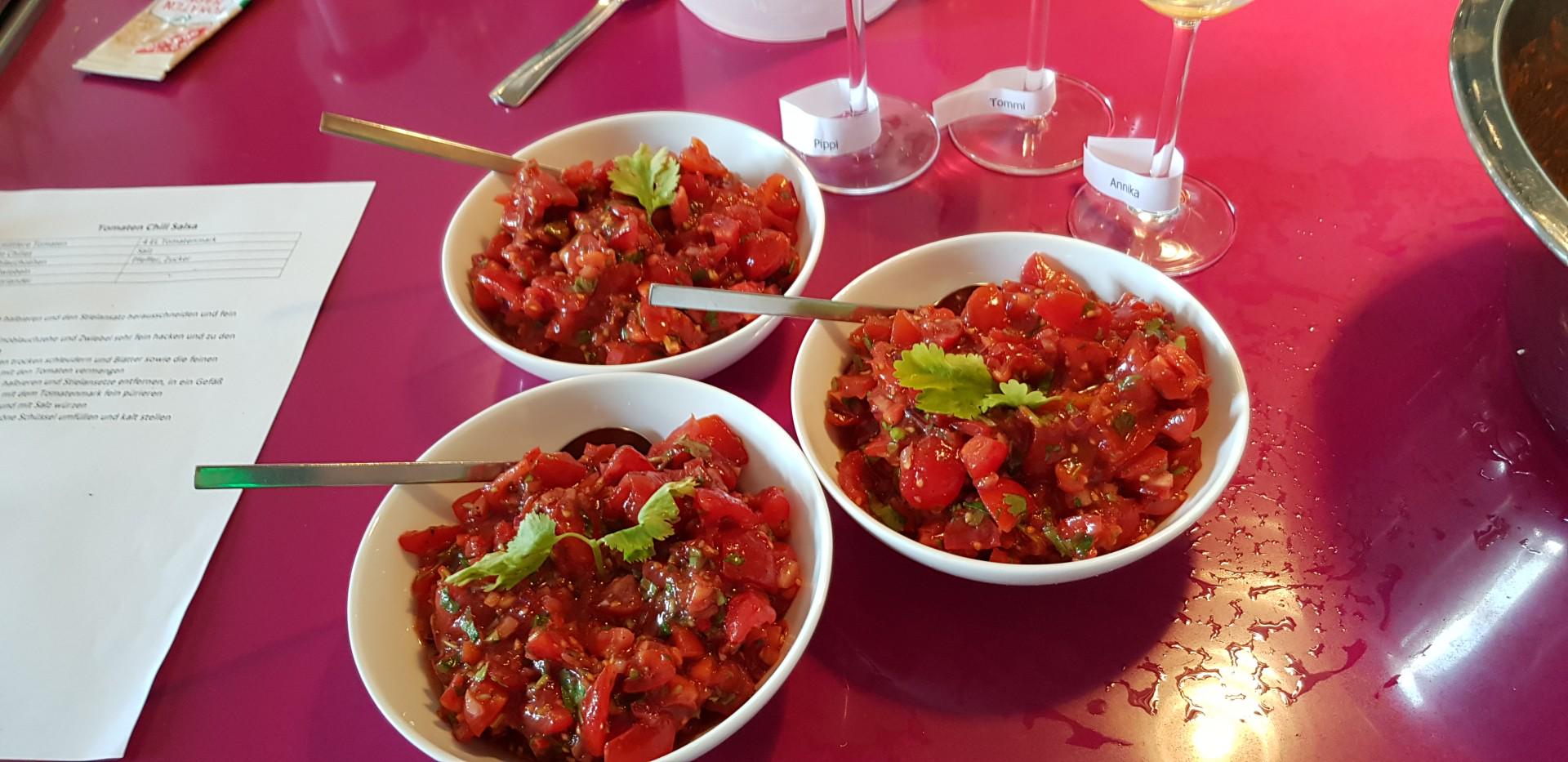 Drei weiße Schalen mit frischer Tomatensalsa auf pinkem Tisch, daneben Weingläser mit Namensschildern.