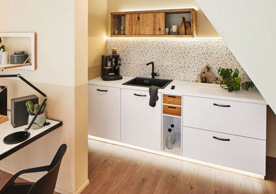 Moderne weiße Küchenzeile mit schwarzer Spüle, Holzregal und LED-Beleuchtung für stilvolle Kücheneinrichtung