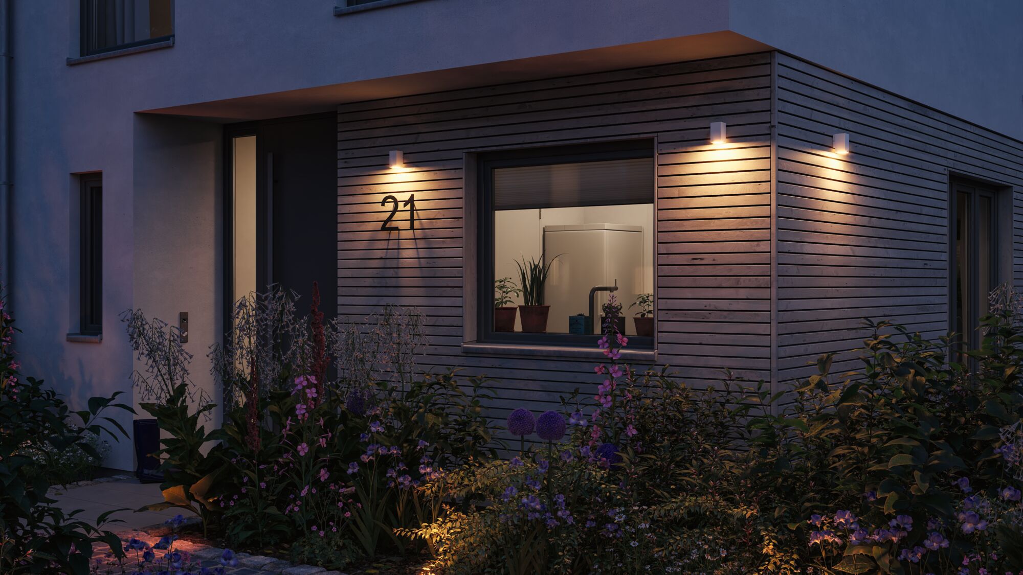 Modern white outdoor wall lights on wooden facade illuminate house number 21 and flower garden at dusk.
