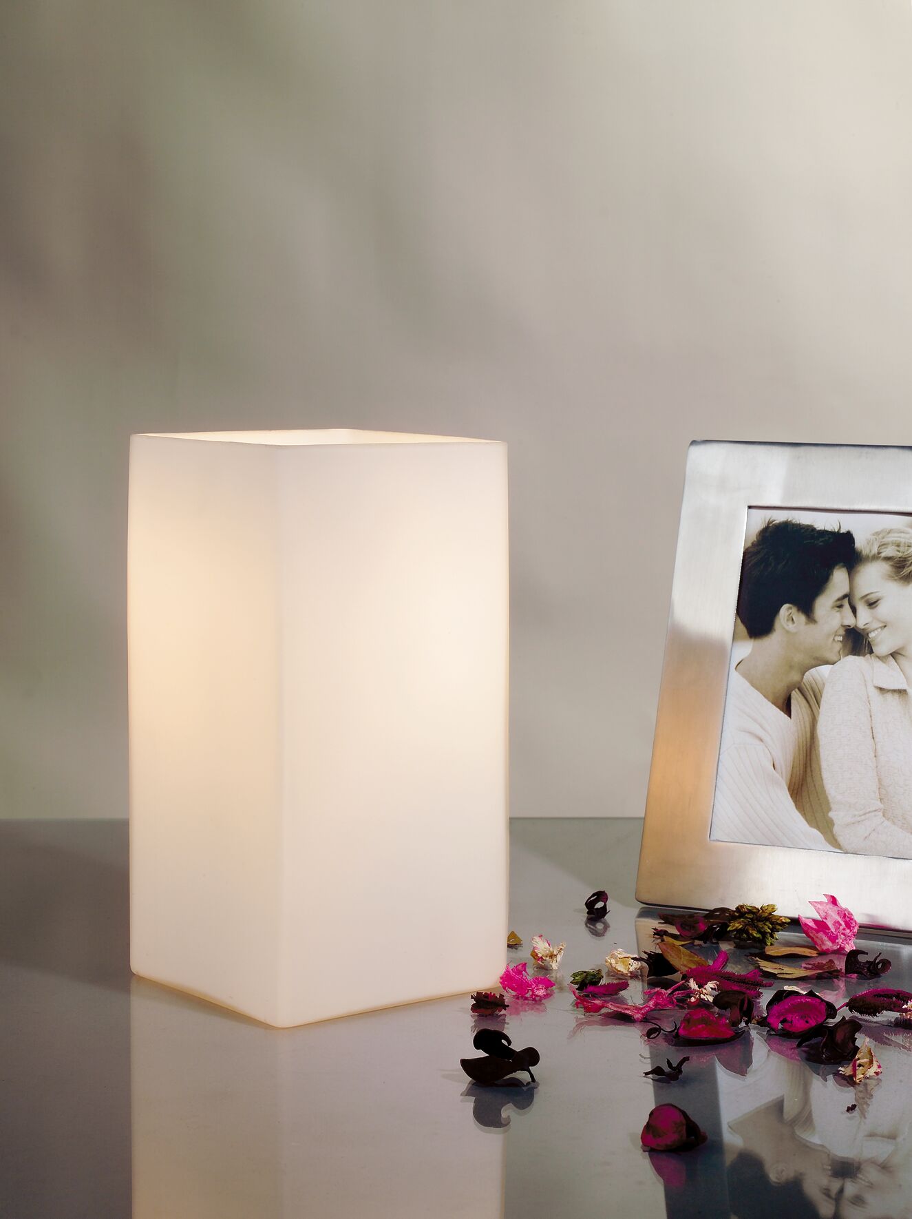 Weiße quadratische Tischleuchte aus Kunststoff mit warmem Licht und dekorativen Blütenblättern.