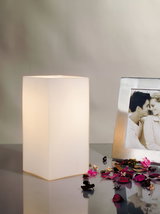 Weiße quadratische Tischleuchte aus Kunststoff mit warmem Licht und dekorativen Blütenblättern.