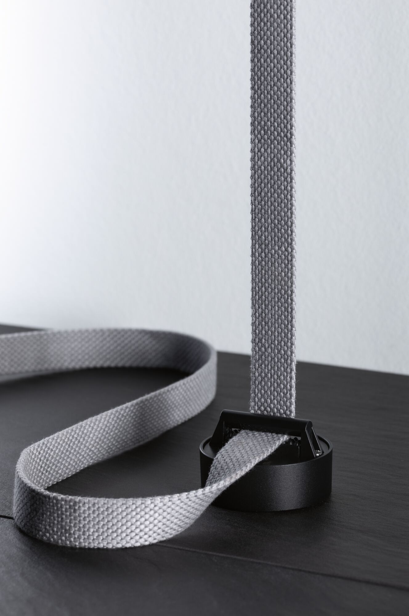 Sangle textile grise avec boucle en plastique noir sur surface sombre pour accessoire d'éclairage.