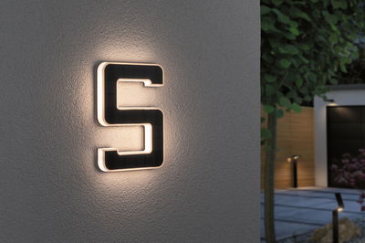 Illuminated house number 5 in black material with warm white LED light on gray outdoor wall