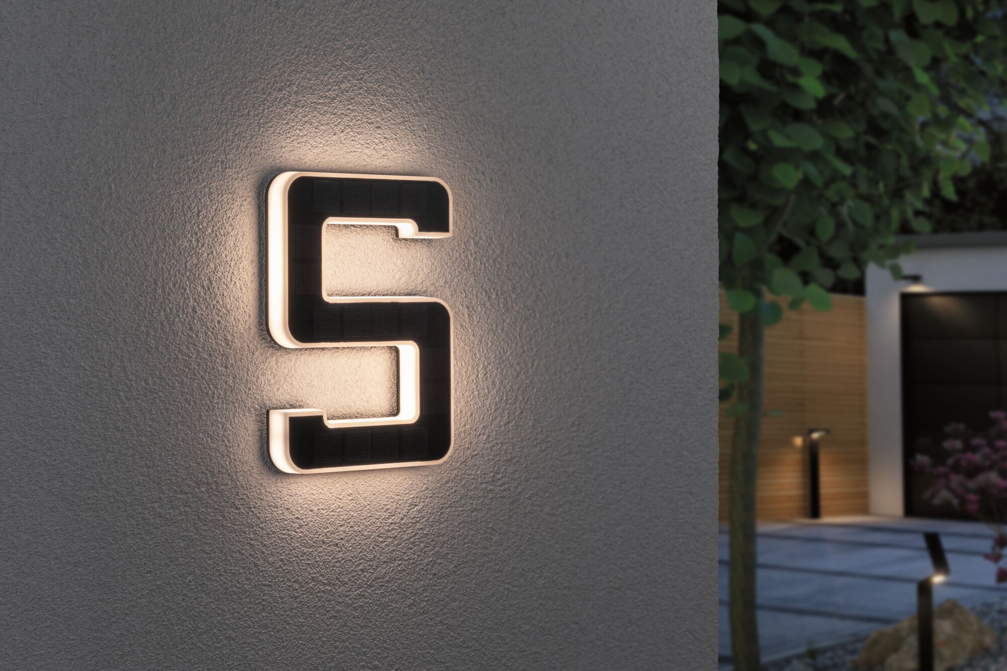 Schwarze Solarleuchte in S-Form mit warmweißem LED-Licht an grauer Wand für Außenbeleuchtung